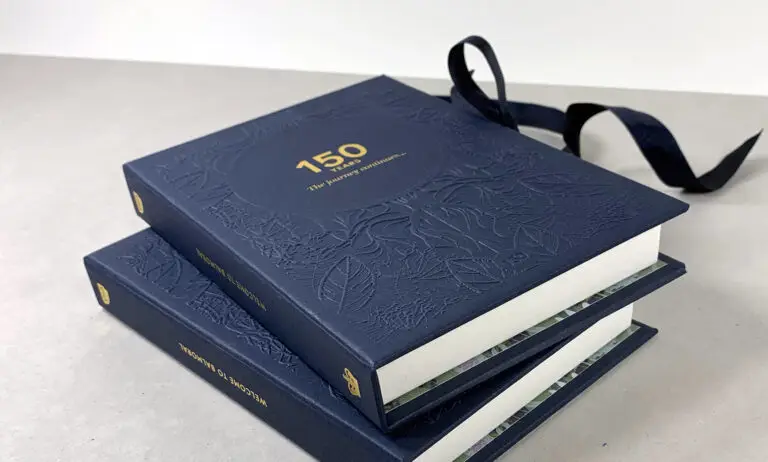 VSA boxed book invitation with blind embossed foiled hard back cover and ribbon closure.